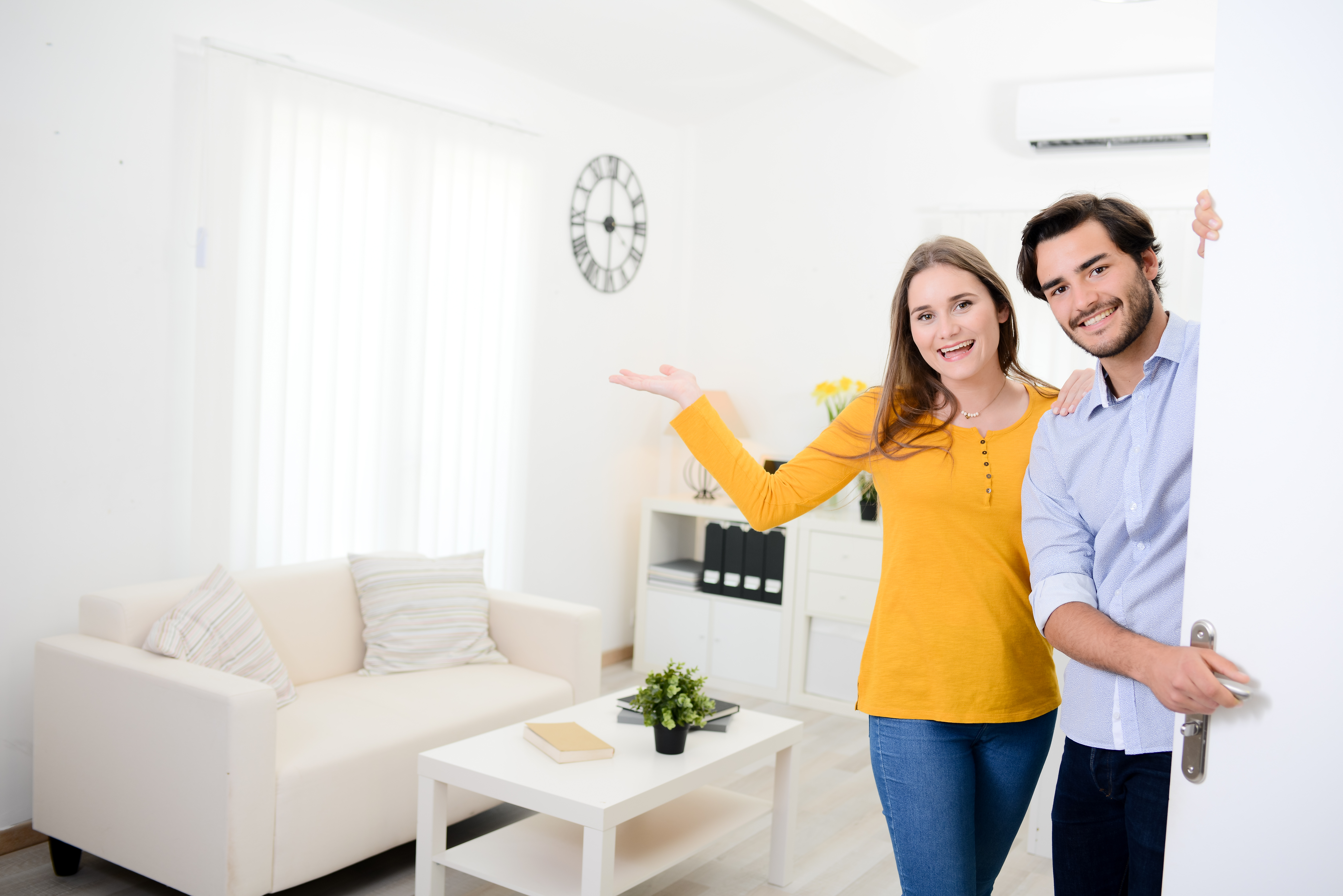 cheerful young couple man and woman welcome  at open front door new home apartment